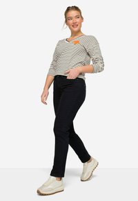 Maglietta a maniche lunghe a righe con scollo a V e accent torte arancioni, abbinata a jeans skinny scuri e sneakers chiare con suola testurizzata.