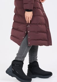 Bordeaux pufferjakke med trykknapper, parret med sorte isolerede ankelstøvler med pelsfor og struktureret sål, båret over grå jeans.