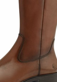 Brown leather ankle boot with elastic side panels, smooth texture, and a slight heel. Features decorative stitching and brand logo detail.