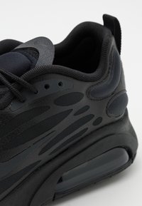 Svart atletisk sneakers med en texturerad ovandel, nätpaneler och en dämpad sula med en synlig luftkammare. Böjd design och släta accenter.