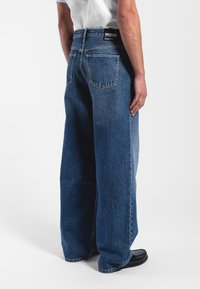 Wide-leg blue denim jeans with a high waist, featuring two back pockets, a black branded label, and subtle fading on the fabric.