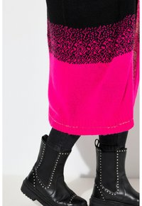 Strickpullover mit abwechselnden Streifen in Schwarz und Pink sowie einem gemusterten Abschnitt; kombiniert mit schwarzen, studierten Stiefeletten und dunklen Jeans.