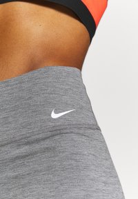 Szare legginsy sportowe z wysokim stanem, z subtelną heatherową fakturą i białym logo Nike na biodrze.