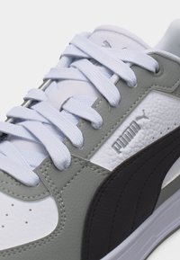 Λευκό και γκρι αθλητικό παπούτσι Puma με λευκά κορδόνια και υφασμένη μαύρη λωρίδα στο πλάι, εμφανίζει ανάγλυφο λογότυπο Puma σε υφασμένο δερμάτινο πάνελ.