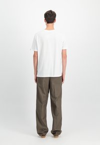 Tricou alb din bumbac cu guler rotund, mâneci scurte și o croială lejeră, asortat cu pantaloni maro lejeri și pantofi de culoare deschisă.