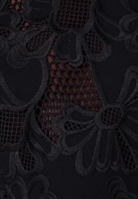 Černá tkanina s propracovanou květinovou výšivkou a síťovými detaily, která zobrazuje směs texturovaných vzorů a různých průhledností.