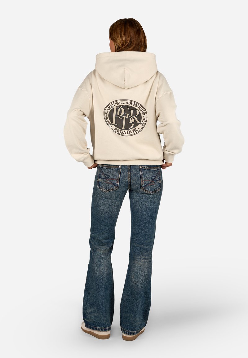 Sweatshirt bege com uma grande gráfica circular preta nas costas. Calças de ganga largas com um lavado azul e costuras detalhadas.