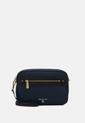 Pequeño bolso bandolera de Michael Kors en azul marino con ribete negro, bolsillo delantero con cremallera y detalles en oro en la cremallera y el logo.