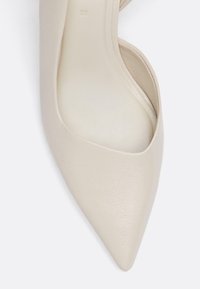 Bež višinčki iz umetnega usnja, z ostrim prstom, teksturirano površino in izrezanimi detajli na straneh. Velikost 37 označena na vložku.