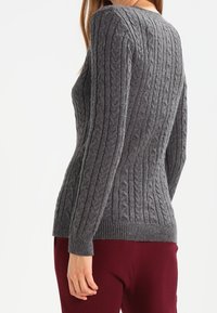 Grå kabelstickad tröja med ribbad nederkant och ärmslut, som har ett strukturerat mönster, kombinerad med bordeauxfärgade byxor.