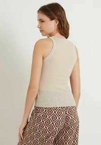 Beige ribbad tanktopp med en figurnära design, rund halsringning och något utsvängd nederdel. Bärs med mönstrade vida byxor.
