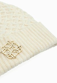 Szydełkowana kremowa czapka beanie z teksturowanym wierzchem, prążkowanym mankietem i złotym akcentem z przodu w formie wplecionego wzoru.