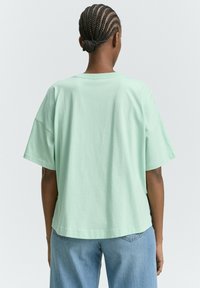 T-shirt oversized verde menta con maniche corte, design a girocollo, texture morbida e vestibilità rilassata, abbinato a jeans blu chiaro.