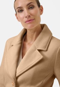 Beige wollen blend jas met een gestructureerde kraag, dubbele knoopsluiting en een zachte textuur, voorzien van een enkele decoratieve knoop.