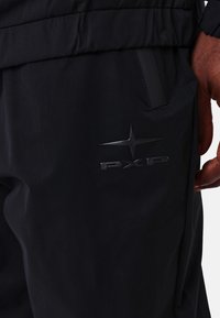Pantalones impermeables negros con textura suave, que cuentan con un bolsillo lateral y un sutil logo PXP en relieve en el muslo. Cintura elástica ajustable.