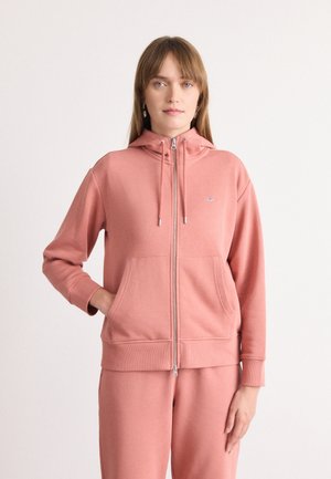 Haut à zip rose en tissu doux, doté d'une poche avant, de cordons de serrage et de poignets côtelés. Détail de logo simple sur la poitrine.