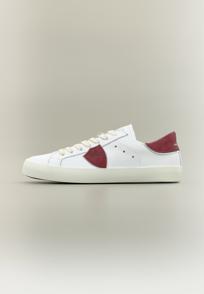 Λευκό δερμάτινο αθλητικό παπούτσι με μπεζ κορδόνια, κόκκινη σουέντ φτέρνα και πλαϊνές επιφάνειες, παρουσιάζεται σε ουδέτερο γκρι φόντο, πλευρική όψη.