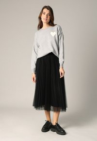 Pull en tricot gris avec un motif de cœur texturé blanc, associé à une jupe en tulle noire et des chaussures noires à lacets.