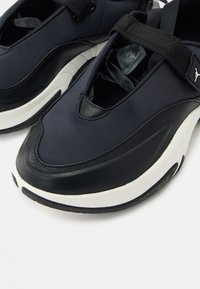 Αθλητικά παπούτσια τύπου slip-on σε ασπρόμαυρο χρώμα με χοντρές σόλες, επενδυμένους γιακάδες και πλεγμένη λωρίδα πάνω από το επάνω μέρος κοντά στον αστράγαλο.