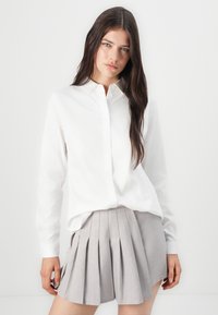 Chemise blanche à manches longues avec col, associée à une mini-jupe plissée gris clair. Tissu lisse avec une coupe ajustée.
