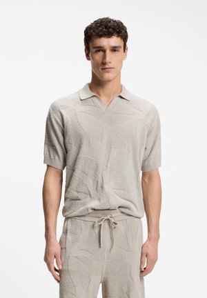 Homme portant un polo à manches courtes texturé beige clair et un short à cordon assorti, debout sur un fond blanc.