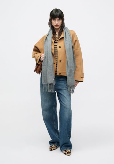 Veste beige oversize, haut marron à rayures verticales, écharpe grise à franges, jean bleu pattes d'éléphant, et escarpins imprimé léopard. Sac à main marron.