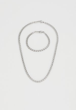 Zilveren metalen sieradenset bestaande uit een kettinghalsketting en een bijpassende armband, beide met vergrendelde schakels en een gepolijste afwerking.