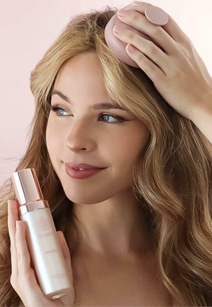 Produit de soin capillaire dans une bouteille blanche élégante avec un accent en or rose. Un applicateur rond de couleur rose pâle est montré tenu contre les cheveux.