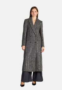 Abrigo largo de doble botonadura hecho de tejido gris texturizado con rayas verticales y detalles de lentejuelas, combinado con pantalones negros de pierna ancha y tacones.