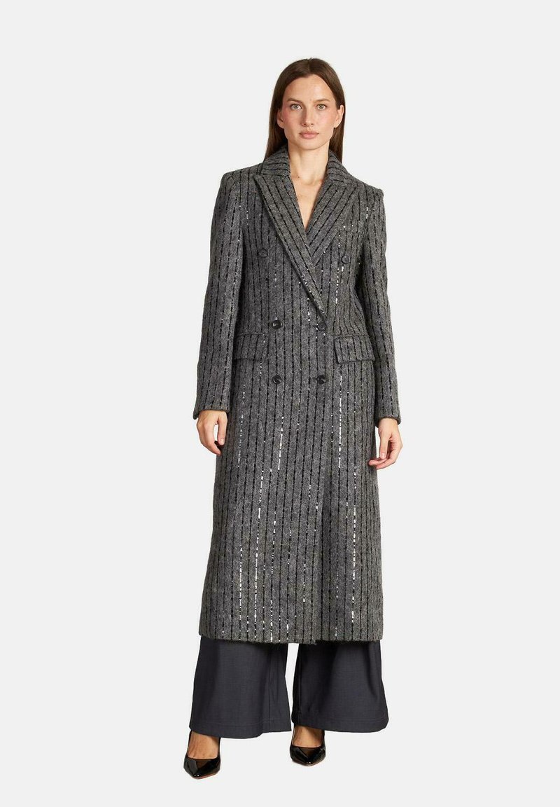 Abrigo largo de doble botonadura hecho de tejido gris texturizado con rayas verticales y detalles de lentejuelas, combinado con pantalones negros de pierna ancha y tacones.