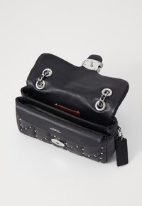 Svart kviltad läderhandväska med silvernitar, kedjehandtag, vredlås och en öppen klaff som visar innerfickan och taggen.