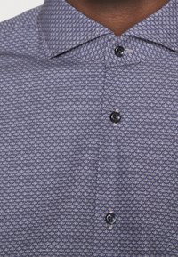 Korte mouwen overhemd in een blauw-witte geometrische patroon, met een puntige kraag en zwarte knopen aan de voorkant.