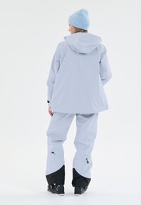 Ljusblå vattentät jacka och byxor, med huva, justerbara manschetter och svarta detaljer vid byxornas nederkant. Slät yta, avslappnad passform.