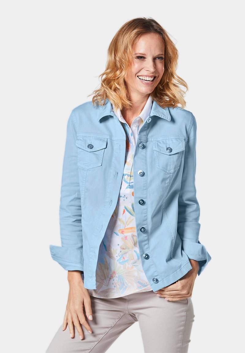 Lichtblauwe button-up jas van gladde stof, met twee borstzakken, opgerolde mouwen en een rechte snit. Draag ik over een gepatterd shirt.