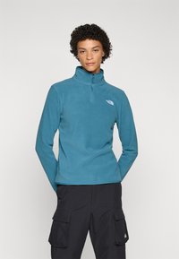 Fleece pullover in teal with a high collar and quarter zipper. Features a white logo on the left chest and long sleeves.