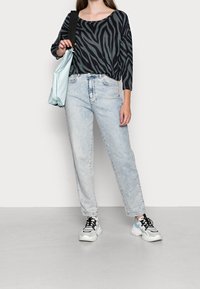 Schwarz-weißes Zebra-Print-Top, hellblaue gerade Jeans, schwarze und weiße Sneakers, hält eine hellblaue Tasche mit einem Schulterriemen.
