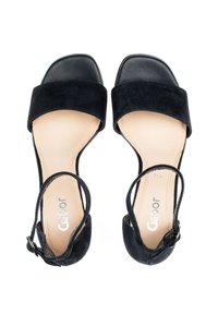 Sandales en suède noir avec une large bride avant, un talon ouvert, une bride de cheville avec boucle, et une semelle en beige lisse. Présente un design à bout carré.