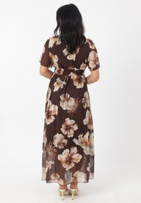 Robe maxi en tissu transparent marron avec de grands motifs floraux beiges et crème. Elle a des manches courtes et une taille smockée.