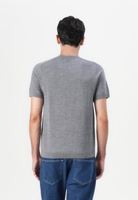 Γκρι κοντομάνικος πουλόβερ με στρογγυλή λαιμόκοψη και λεία υφή. Διαθέτει αθόρυβους ώμους και εφαρμοστή σιλουέτα, συνδυασμένο με μπλε τζιν.