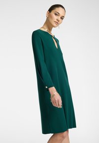 Grünes, langärmliges A-Linien-Kleid mit V-Ausschnitt und Knopfdetails an den Ärmeln, hergestellt aus glattem Stoff. Einfaches, elegantes Design.