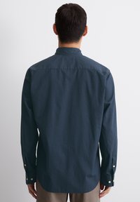 Marineblaues Langarmshirt mit subtiler Textur, geradem Schnitt, Knopfmanschetten und weichem Kragen. Die Rückansicht zeigt ein nahtloses Design und einen lockeren Schnitt.