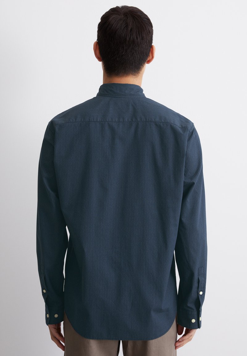 Chemise à manches longues marine avec texture subtile, coupe droite, poignets à boutons et col doux. La vue arrière montre un design sans couture et une coupe décontractée.