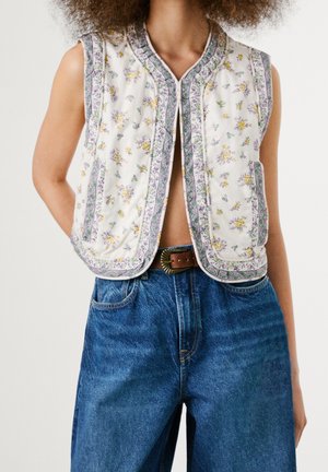 Bezrekawny pikowany kamizelka w kwiaty z fioletowym obszyciem noszona na gołym torsie, w połączeniu z jeansami z wysokim stanem i brązowym paskiem.