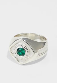 Anel de prata com um topo em formato de diamante, apresentando uma pedra preciosa verde e texto gravado, banda suavemente curva, acabamento polido e detalhes texturizados.