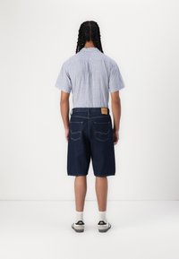 Cămașă cu mâneci scurte, în dungi, de culoare albastru mediu, asociată cu pantaloni scurți din denim de culoare albastru închis. Prezintă o etichetă din piele pe pantaloni scurți și picioare drepte.