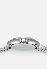 Montre en acier inoxydable argenté avec un boîtier rond, une lunette texturée et un bracelet en maillons. Détail de la couronne visible sur le côté.