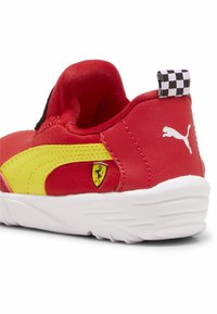 Piros és sárga sportcipő, puha szövet felső résszel, fehér gumitalppal, kockás húzófüllel és Ferrari logóval az oldalon.