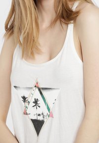 Top bianco a canotta con grafica triangolare che presenta palme e motivi geometrici in tonalità di nero, rosa e turchese. Texture morbida, design informale.