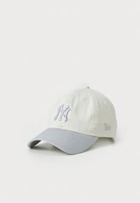 Baseball cap i lys beige med en grå skygge, der har en broderet NY-logo i grå. Lavet af blødt stof med et struktureret design.