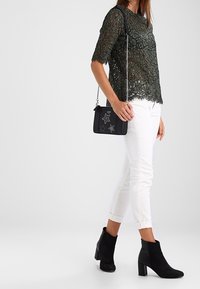 Svart spetslinne med rund hals, vita avkortade byxor och svarta mockaboots, kompletterat med en liten svart handväska med stjärndetaljer.